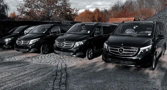 Quatre vans Mercedes noirs alignés sur une cour pavée.